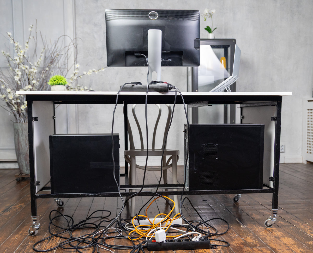 Modern office desk with computer setup and scattered cables in a room.