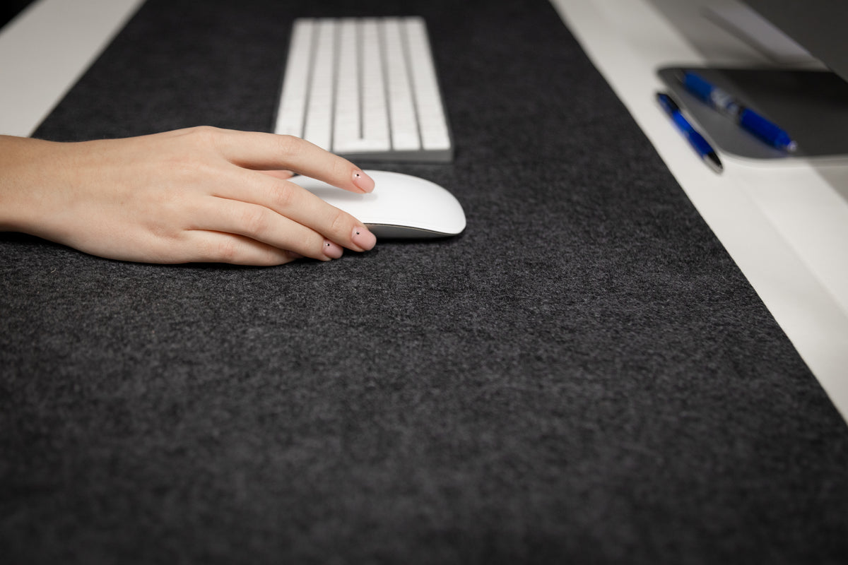 Hand using a computer mouse on a dark desk with a keyboard in the background